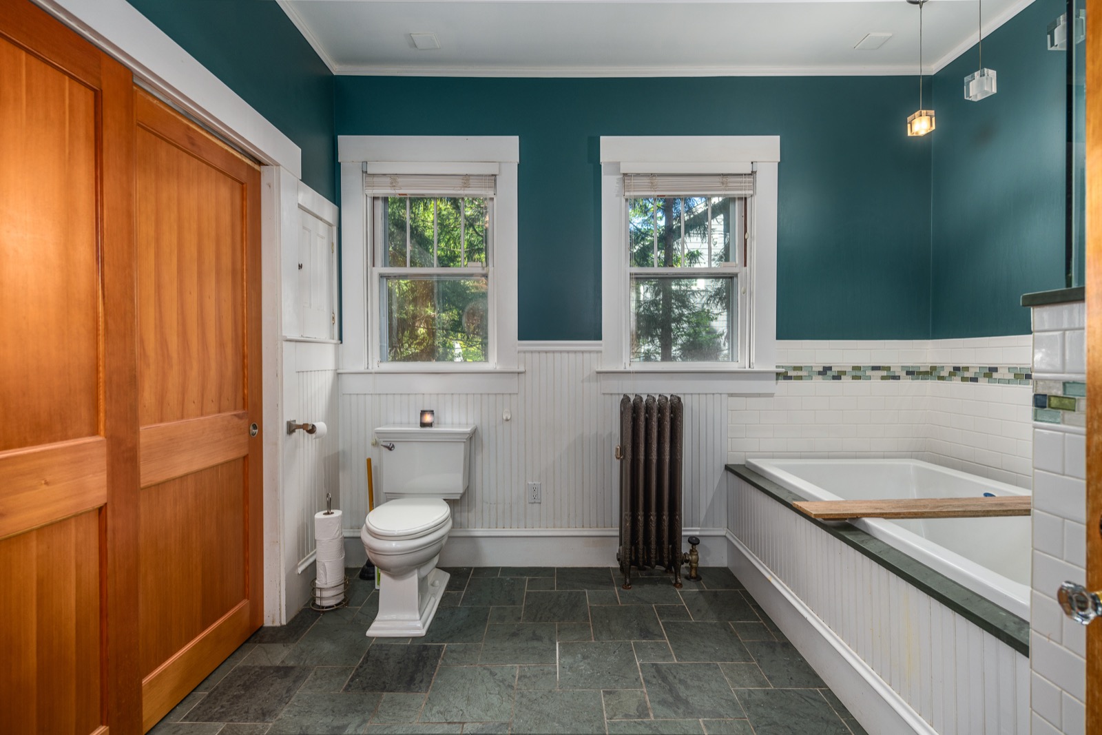 Main bathroom with deep teal walls, slate floor, jacuzzi tub, and beadboard wainscoting.