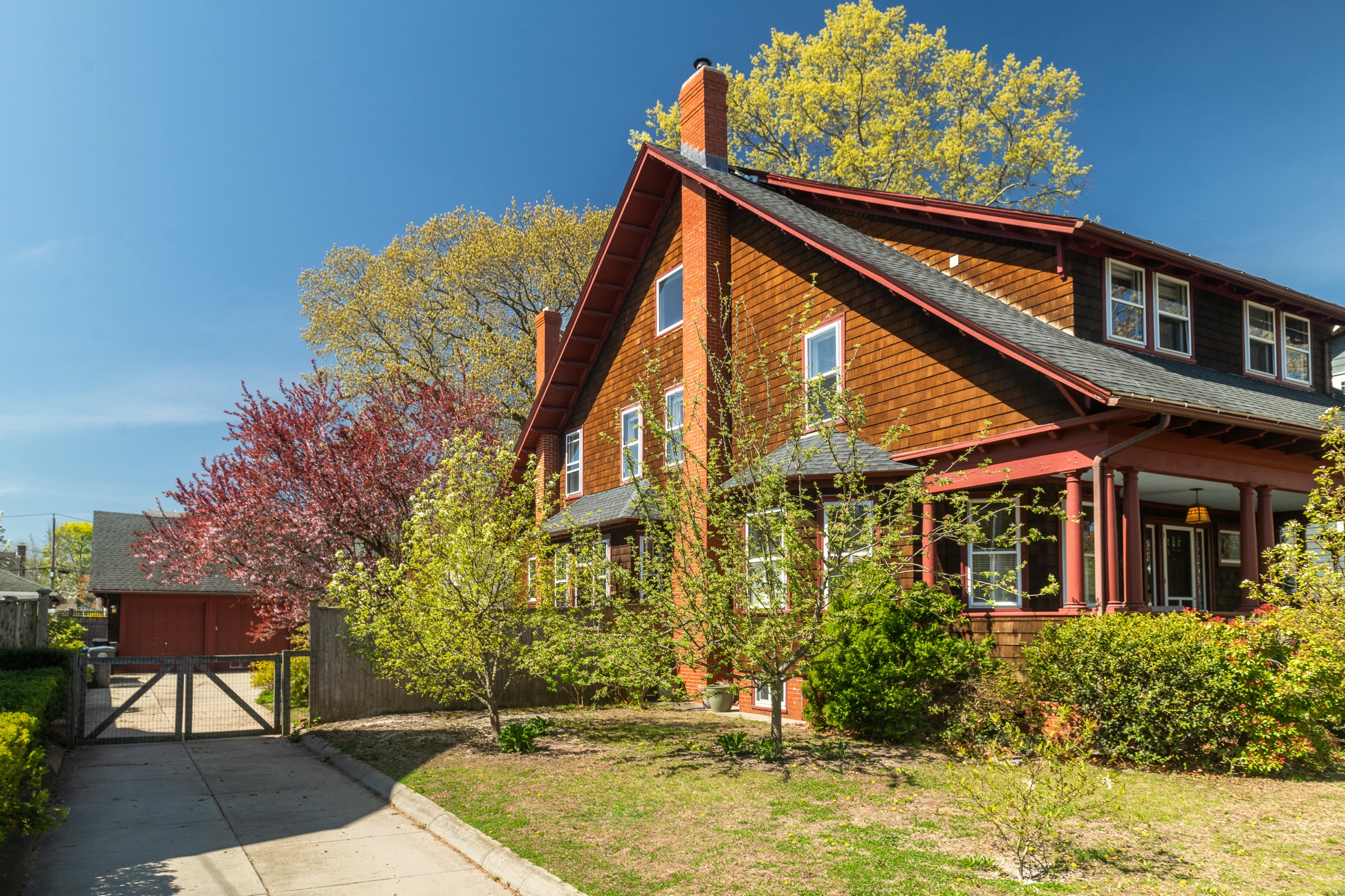 Side view of the Wheeler Lodge — a 1900 Arts and Crafts bungalow with a tall central peak and chimney, framed by a flowering cherry tree and spring foliage.