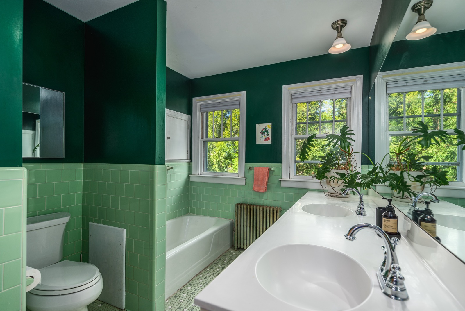 Second full bath with deep green walls, vintage green tile, and a double vanity.