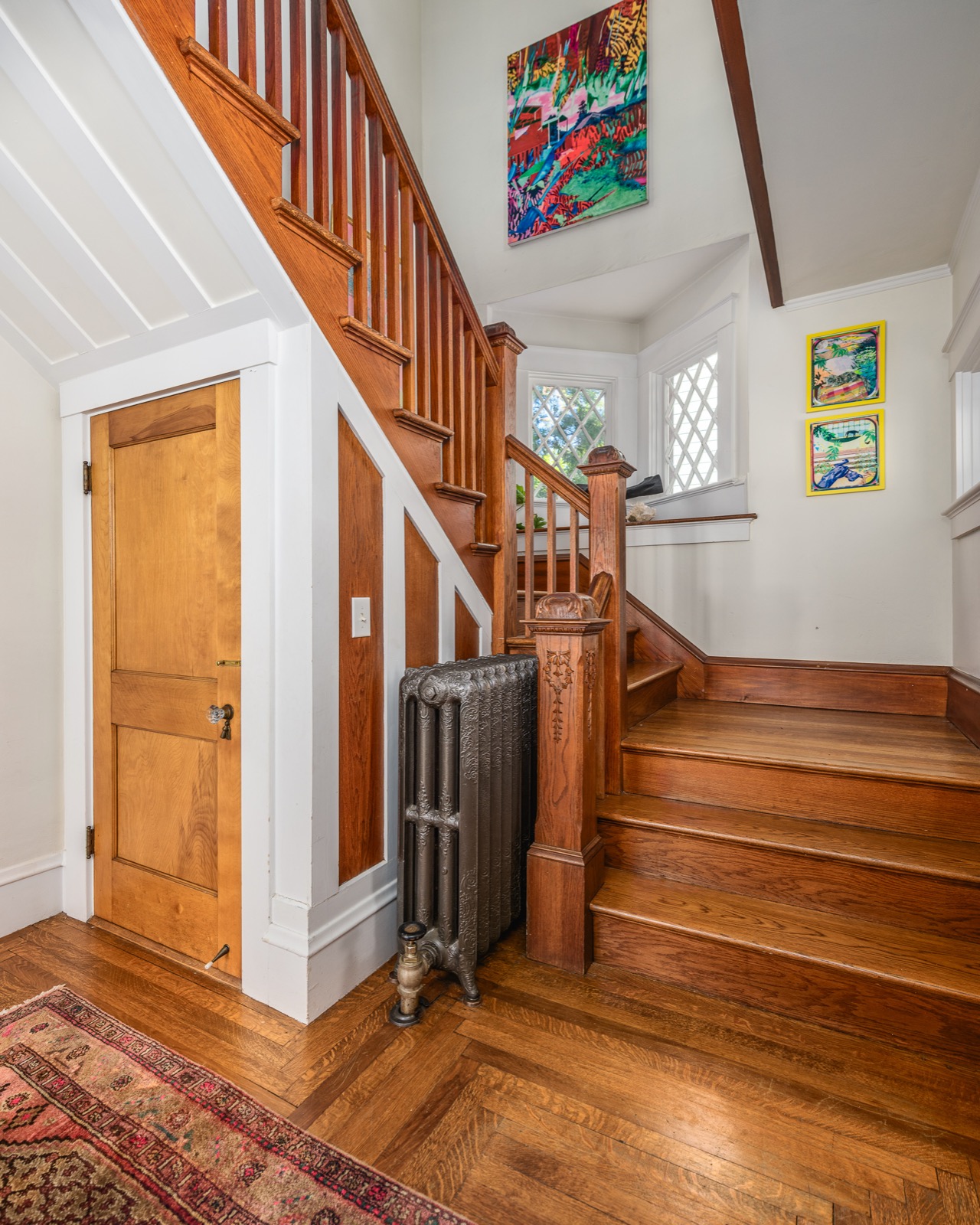 Main staircase with original quarter-sawn oak treads, leaded-glass window, and cast-iron radiator.